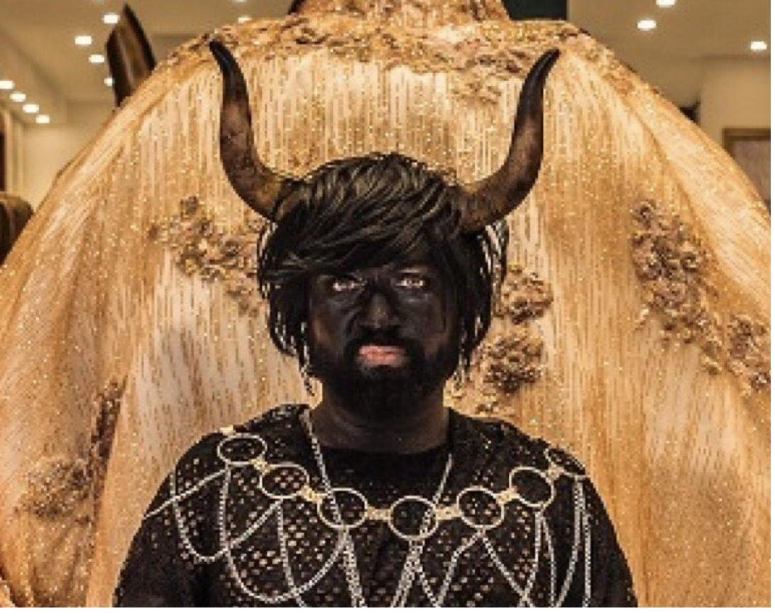 Cabaret Silencio with gold wings, black horns, and layered silver chain necklaces against a gold background.