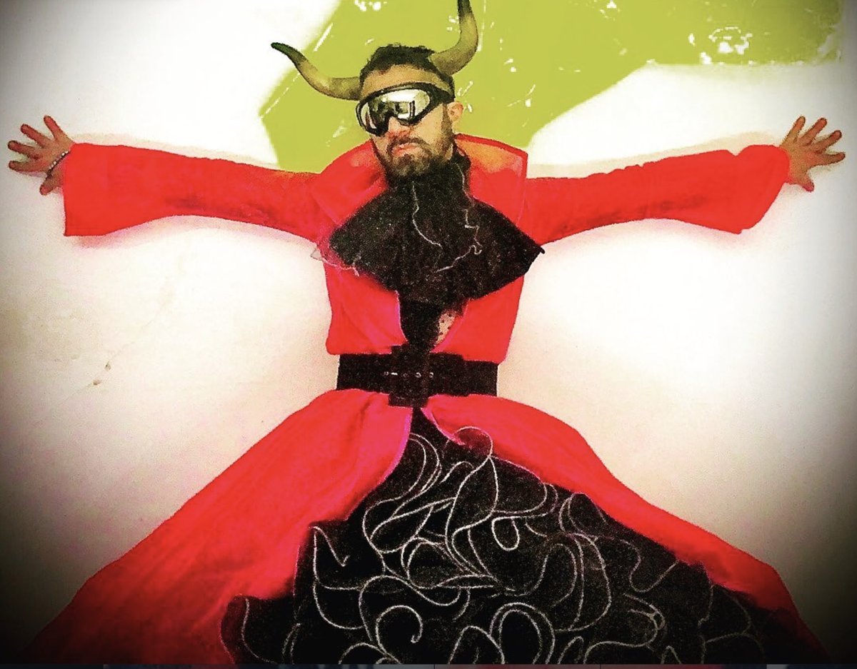 Studio portrait of Cabaret Silencio in a red kimono, horns, and an embroidered black skirt, against a white backdrop with a lime-green paint splash.